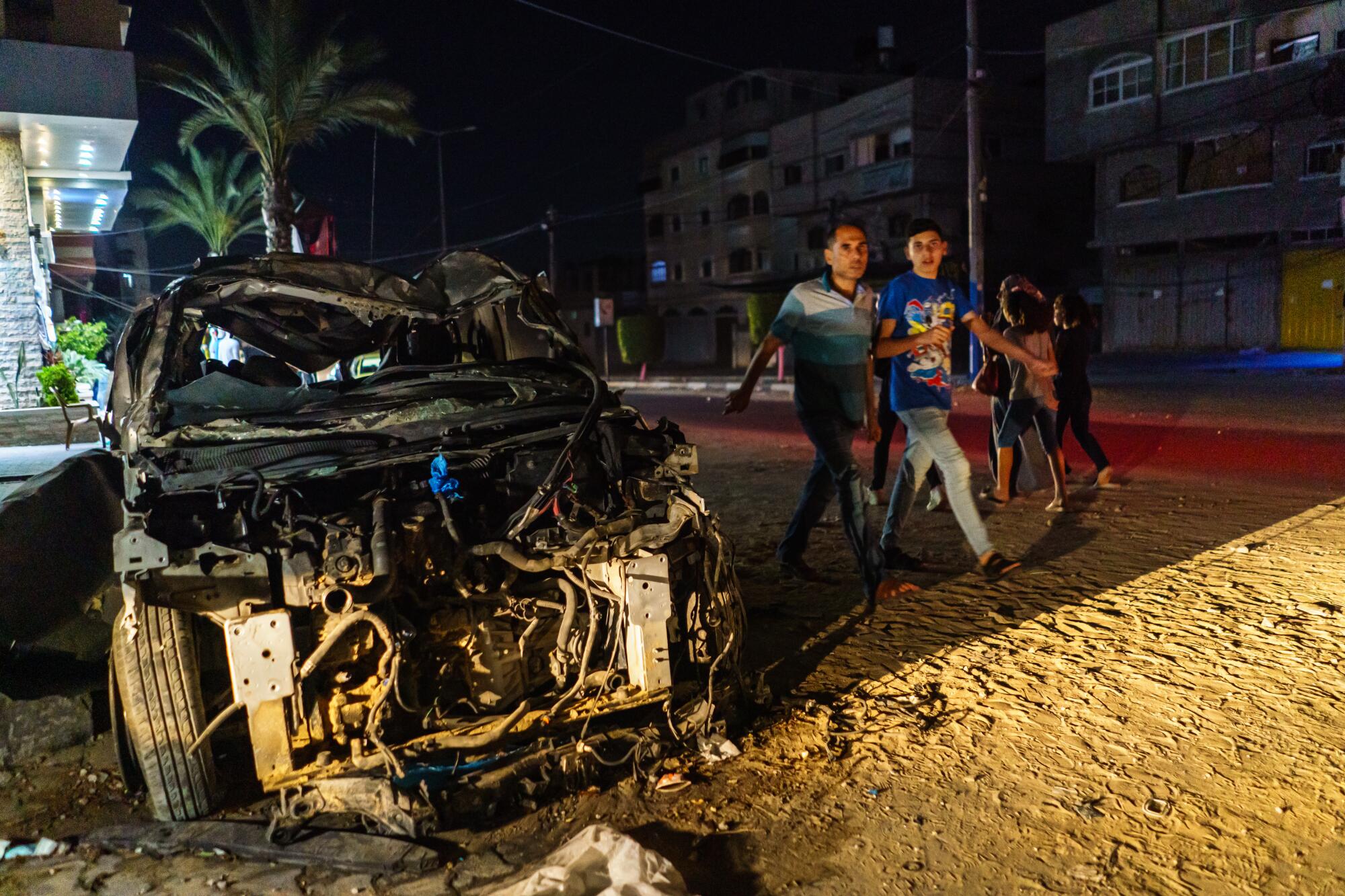 Palestinian pedestrians near a bombed-out car in Gaza City