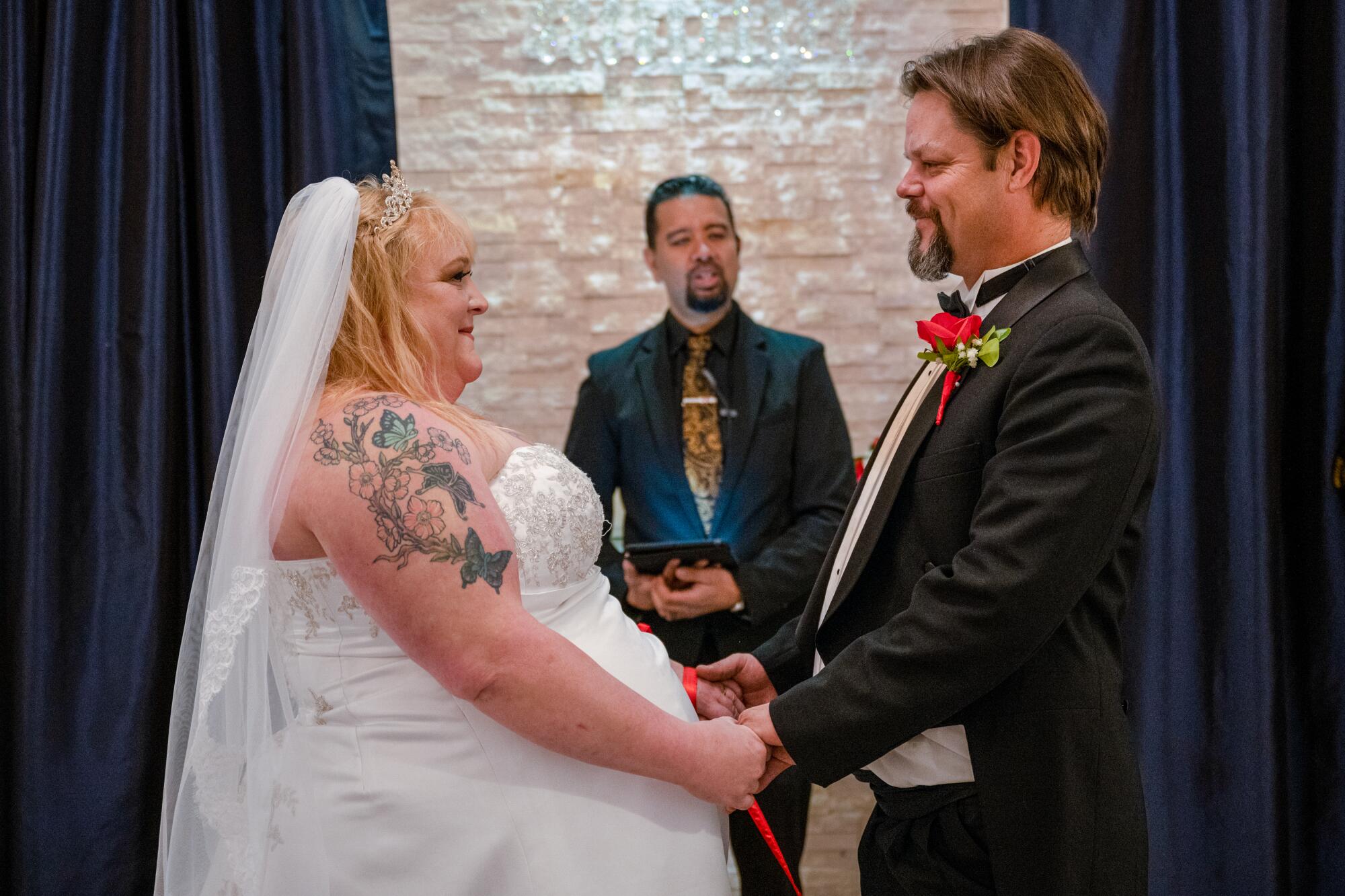 A couple in traditional wedding dress hold hands and face each other