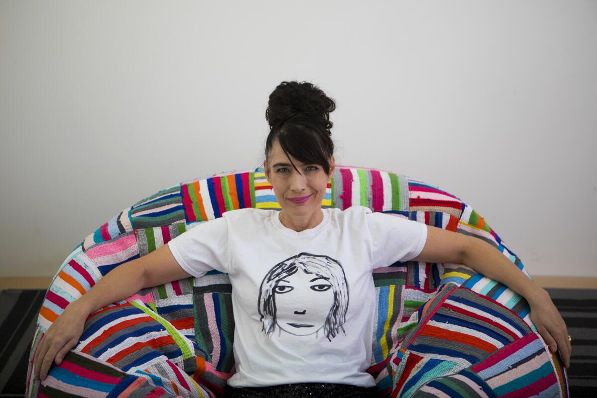 A woman in a white T-shirt with a drawing of a face on it sits on a multicolored chair