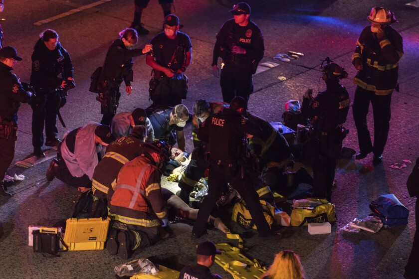 Emergency workers tend to an injured person on the ground after a driver sped through a protest-related closure on the Interstate 5 freeway in Seattle, authorities said early Saturday, July 4, 2020. Dawit Kelete, 27, has been arrested and booked on two counts of vehicular assault. (James Anderson via AP)
