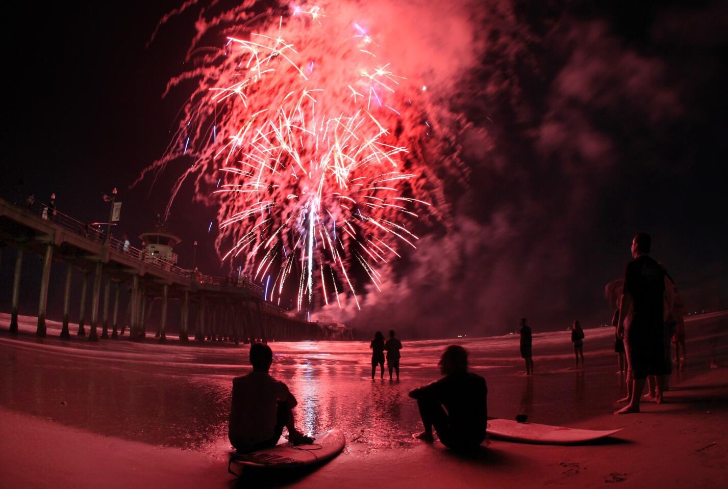 Independence Day surfers Breden Salstrom, left, and Omar Haddad, both of Huntington Beach, watch fireworks launched from the Huntington Beach pier.