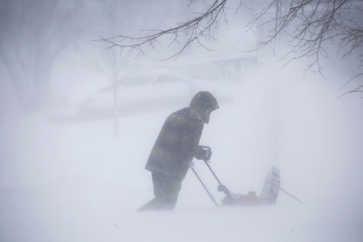 A person partly obscured by a blizzard uses a snow blower to clear a path.