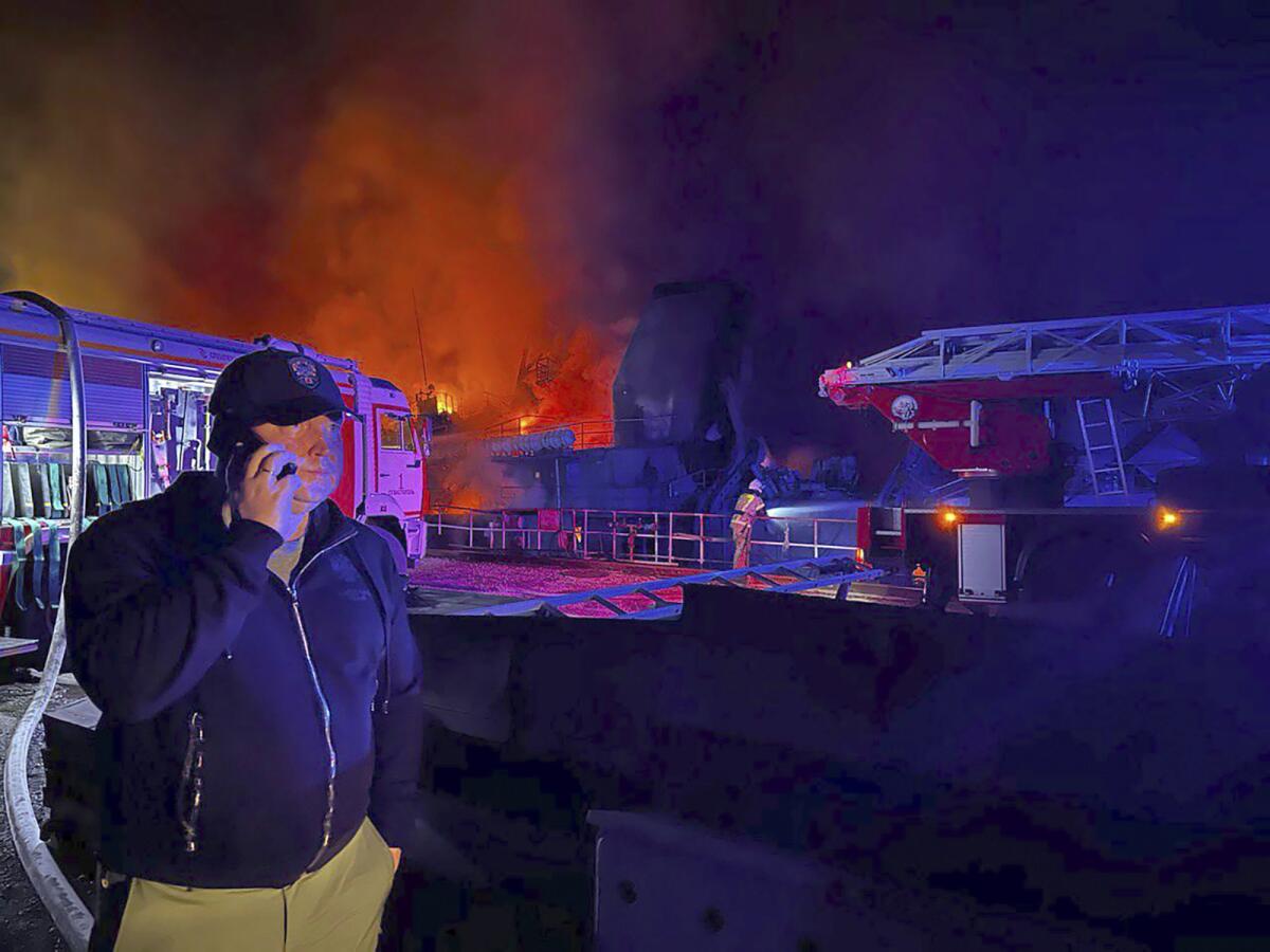 Sevastopol Gov. Mikhail Razvozhaev speaks on a phone as smoke and flame rise in the background.