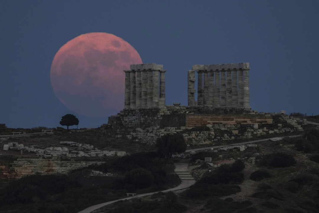 The full moon rises behind Greek ruins.