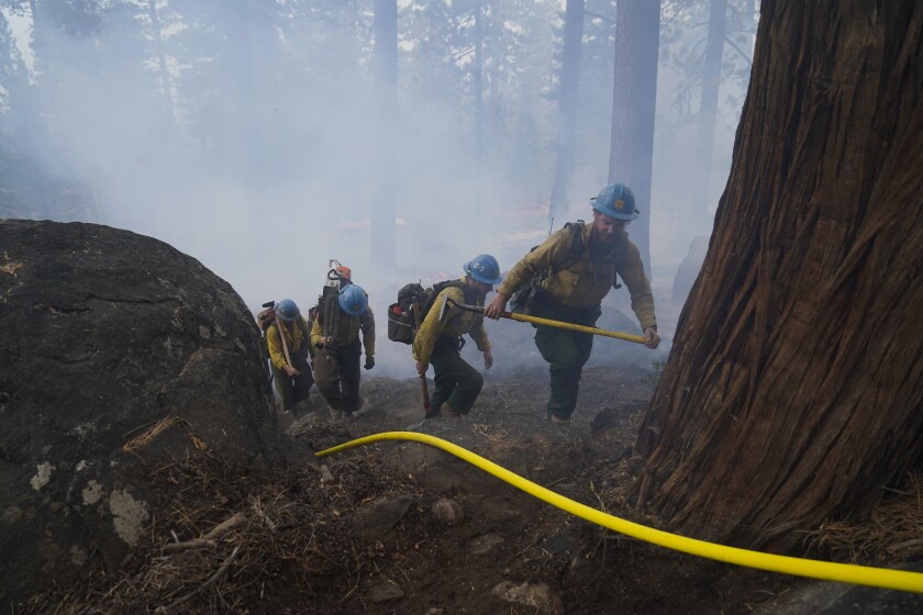 Firefighters hike up a forested mountain amid a haze of wildfire.