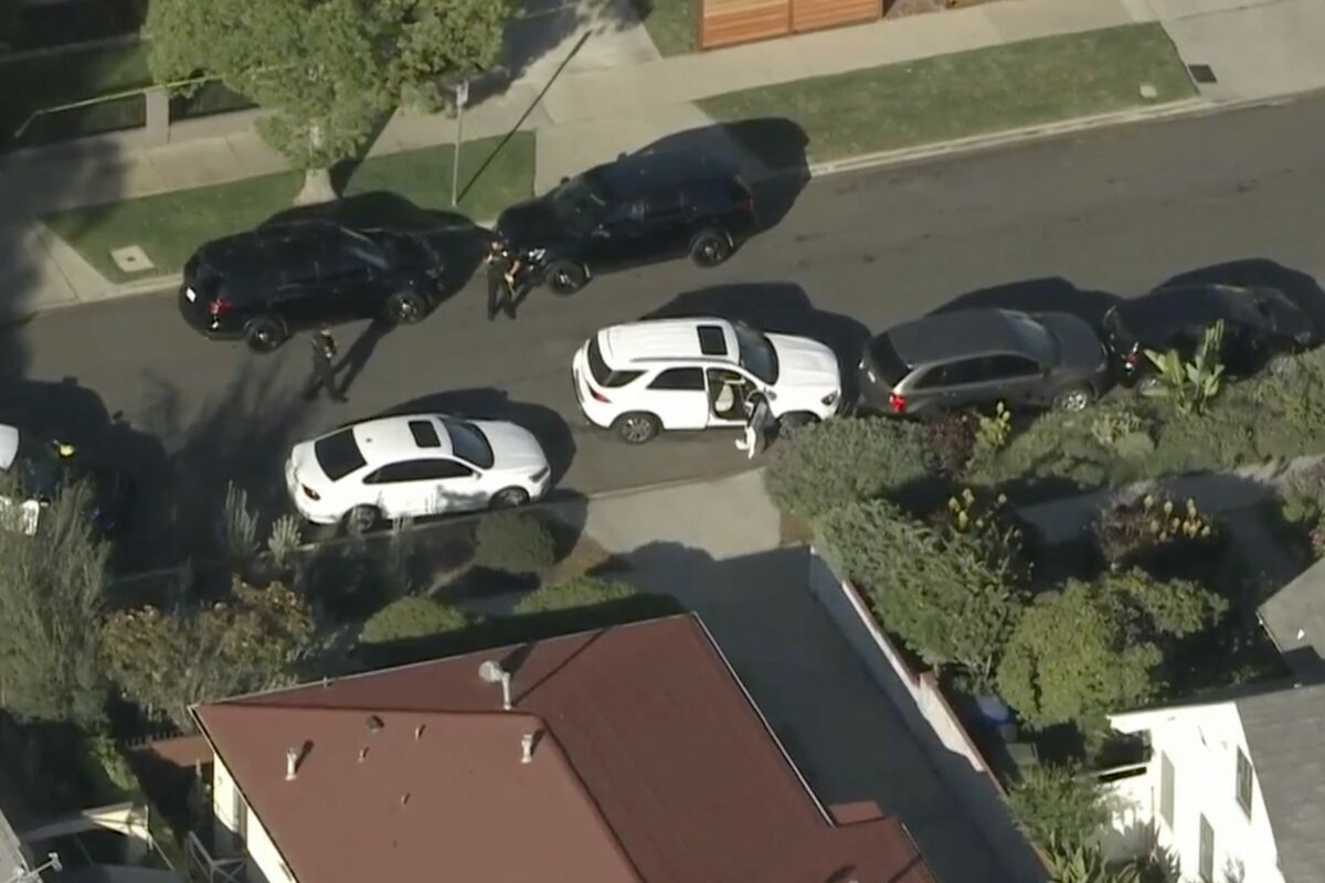 Aerial view of police officers around a white SUV with its doors open that crashed into a parked car.