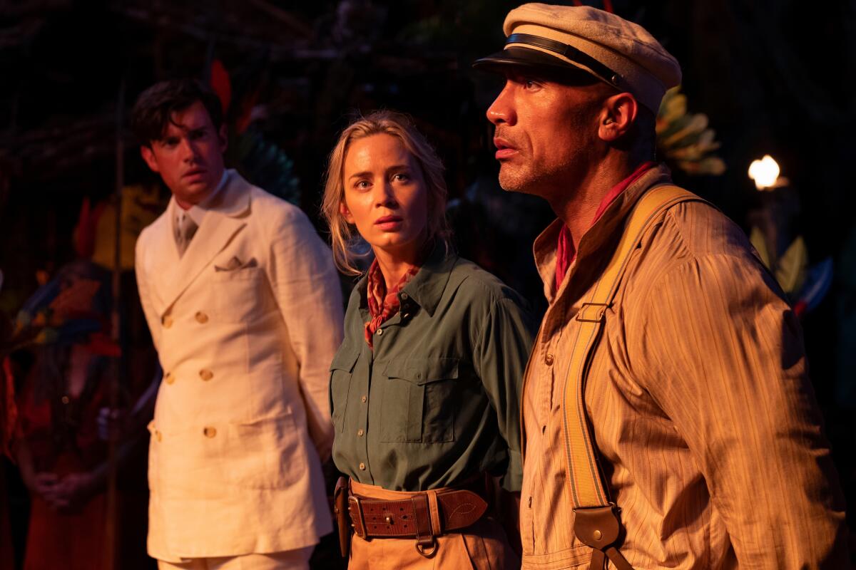 A man in suspenders and a cap, right, looks forward while a man and a woman look at him 