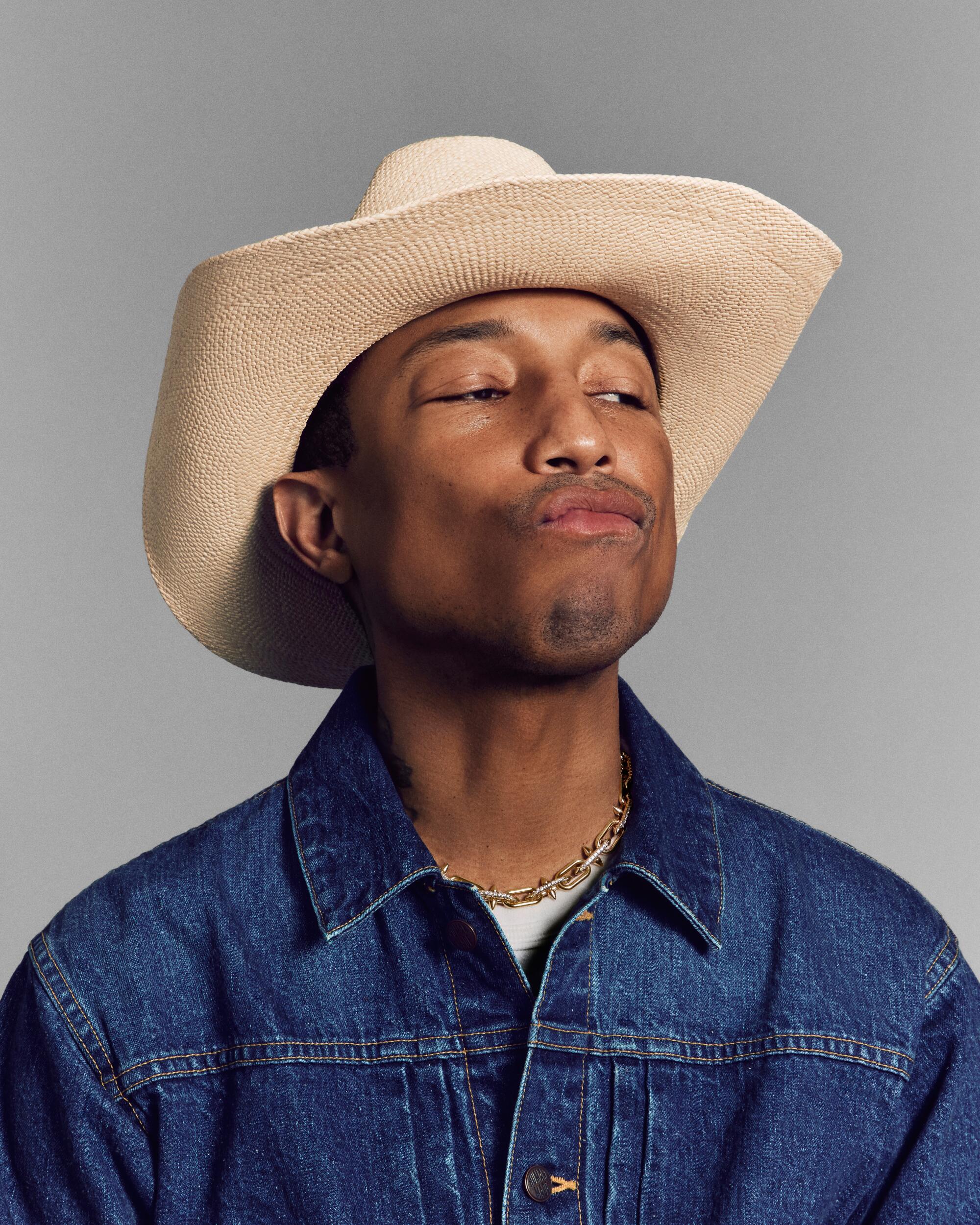 Pharrell Williams in a cowboy hat and denim shirt, pursing his lips