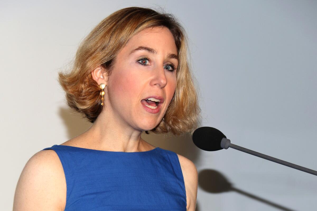 A woman in a blue dress speaks into a microphone