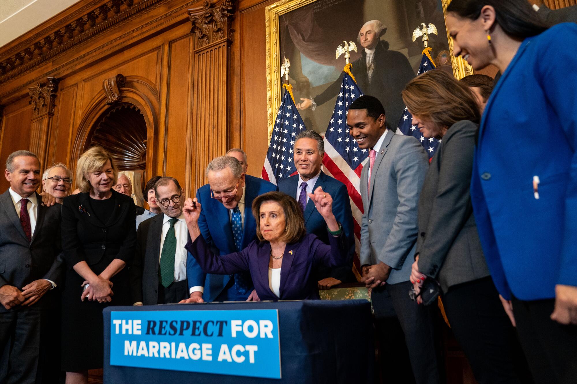 Lawmakers surround Speaker Nancy Pelosi, raising her fists from a desk with a banner reading, "The Respect for Marriage Act."