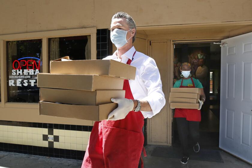 California Gov. Gavin Newsom, carries meals made at the Queen Sheba Ethiopian Cuisine restaurant, to a waiting delivery vehicle in Sacramento, Calif., Friday, June 19, 2020. Newsom, visited the restaurant, owned by Zion Taddese, right, that is participating in the Great Plates Delivered program that provides meals to older adults who are at-risk to COVID-19. (AP Photo/Rich Pedroncelli, Pool)