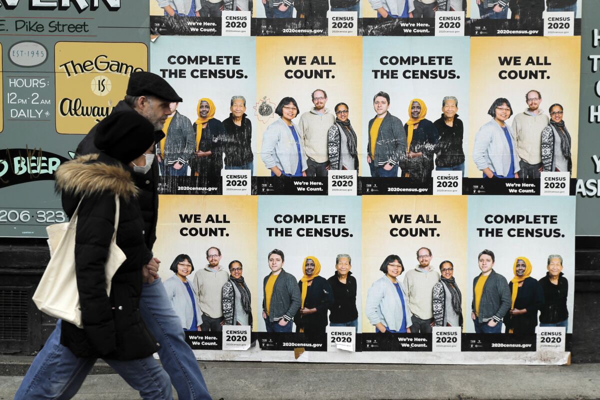 People walk past Census 2020 posters on a wall that say Complete the census, we all count.