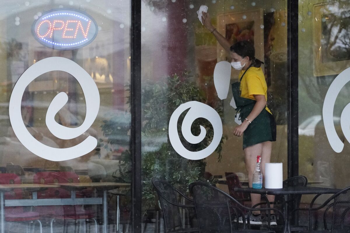 In this June 24, 2021 photo, an employee wears a mask as she cleans exterior windows at an ice cream & yogurt store in Buffalo Grove, Ill. Growth in the U.S. services sector, where most Americans work, increased to a record pace in July even as businesses continued to face challenges in hiring workers. The Institute for Supply Management reported Wednesday, Aug. 4, that its monthly survey of service industries rose to a reading of 64.1 in July, up from 60.1 in June. (AP Photo/Nam Y. Huh)