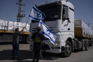 Personas con banderas israelíes frente a camiones dirigidos a llevar ayuda humanitaria a la Franja de Gaza, en el cruce Kerem Shalom, el 9 de mayo de 2024. (Foto AP/Leo Correa)