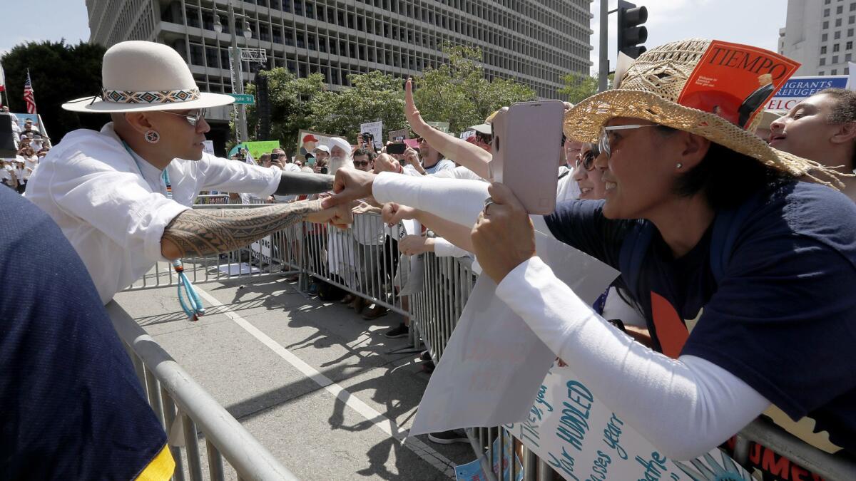 Jimmy “Taboo” Gomez, left, a member of the pop group the Black Eyed Peas, greets protesters after performing at the Families Belong Together rally in L.A.