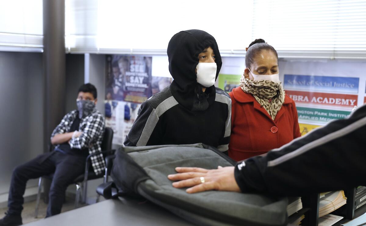 Tenth-grader Fredy Rubio, 16, center, and his mother, Carolyn Chavez, pick up a laptop last week at Linda Esperanza Marquez High School in Huntington Park for schoolwork at home.