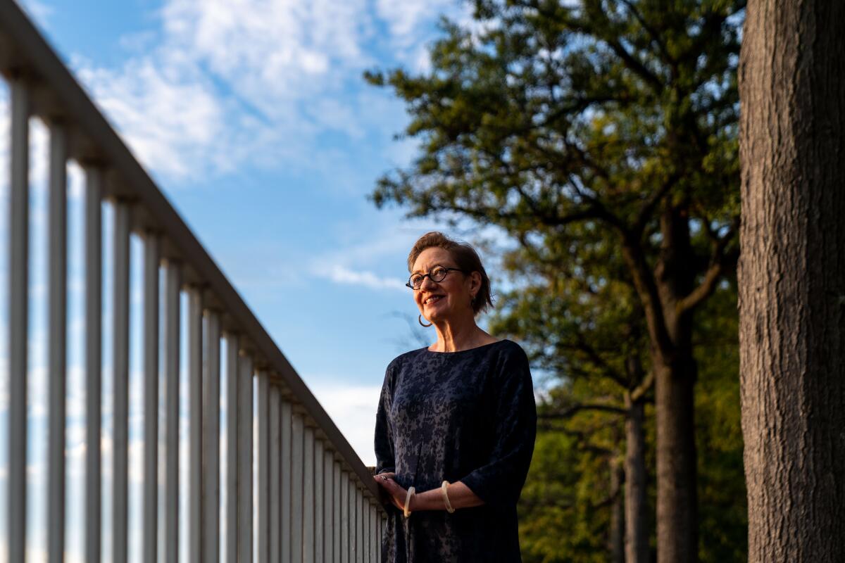 Nina Olson leans on a rail with a stand of trees behind her