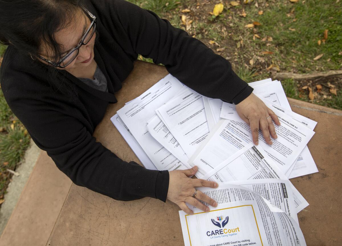A women sits at a table outside with numerous paper documents spread out.