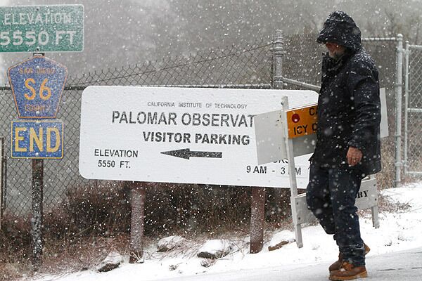 A maintenance worker prepares to set up a road sign announcing that Palomar Observatory is closed. The area experienced snow and icy roads with the latest storm. See full story