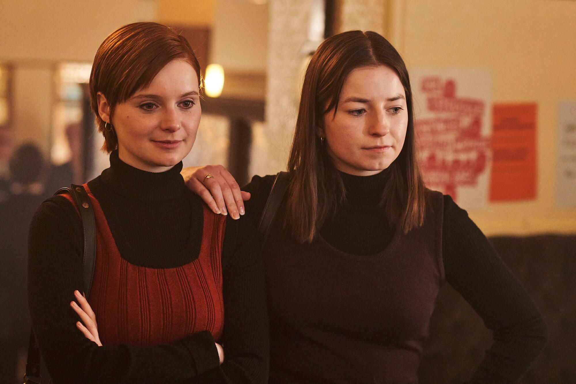 Two women in dark clothing stand and look downward.