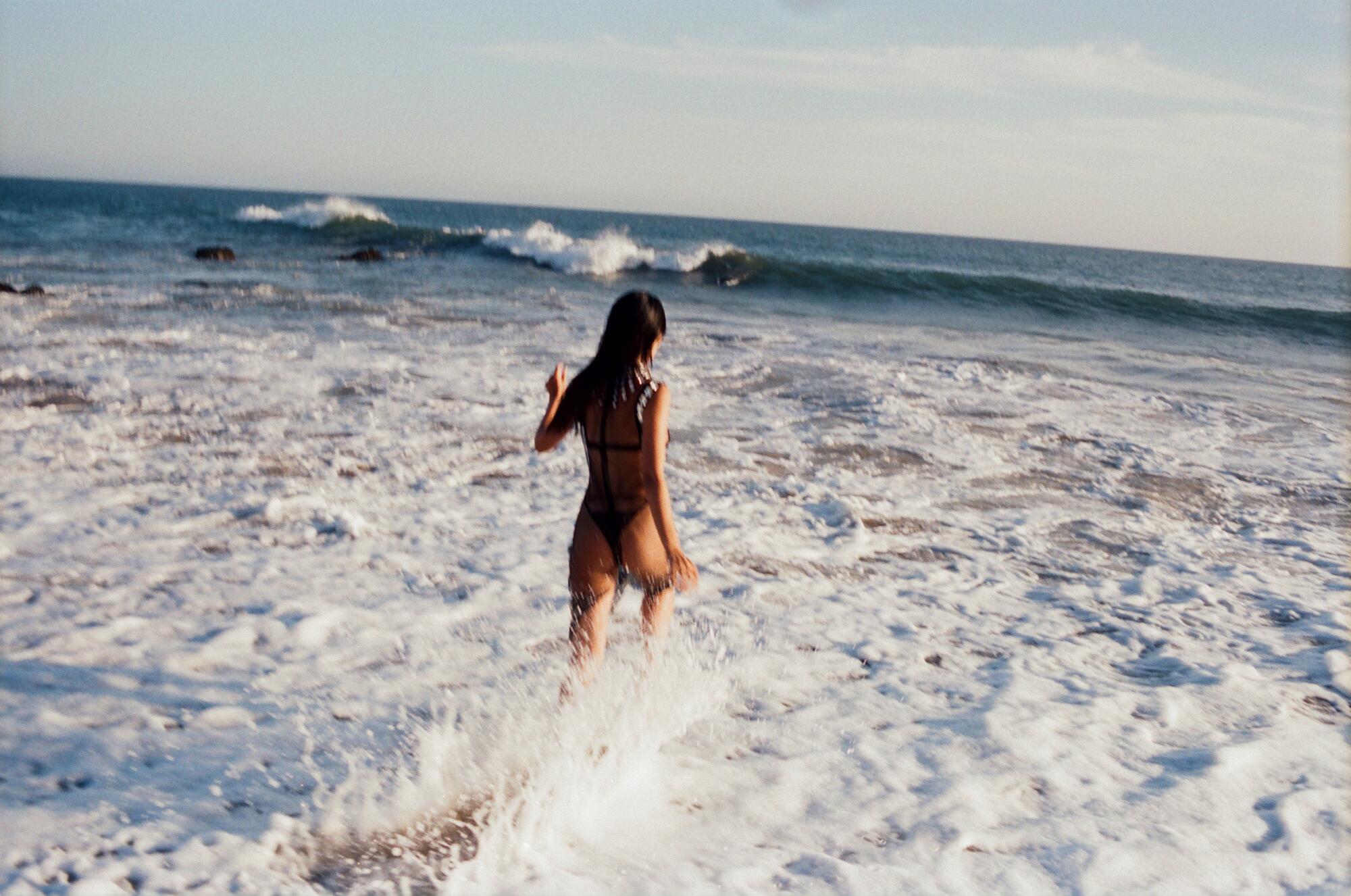 A woman in lingerie runs into the ocean.