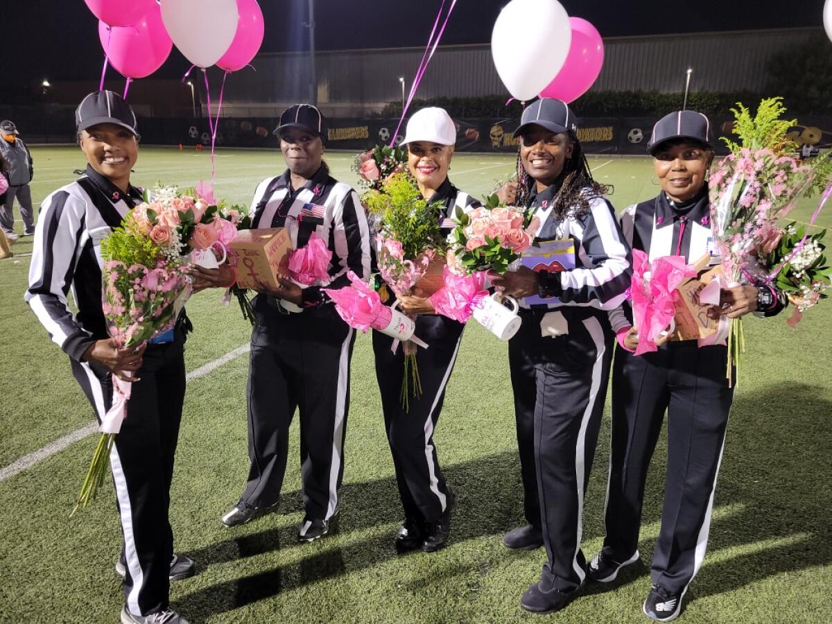 Five women pose for a photo with flowers and balloons on a football field.