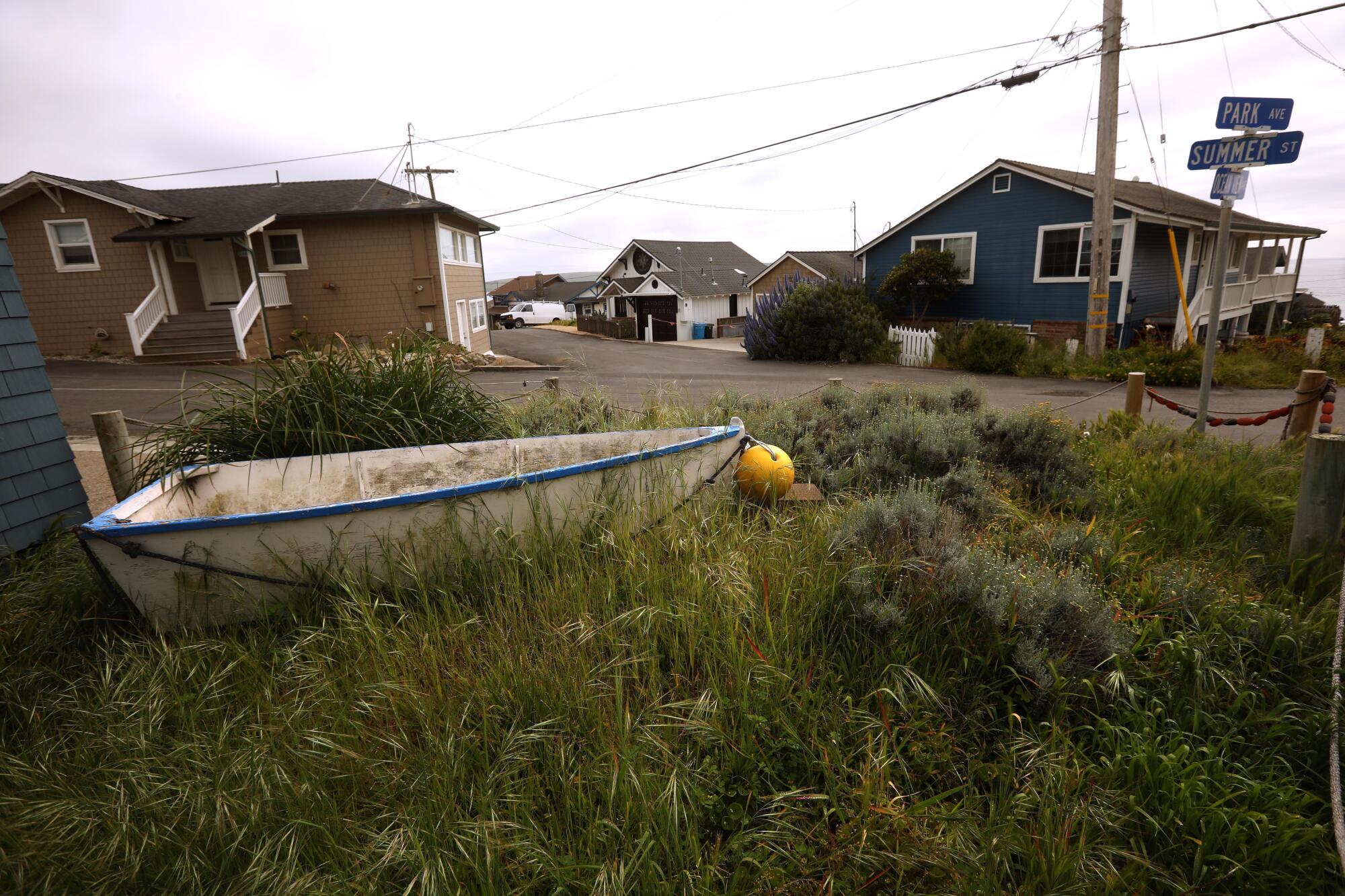 A small boat rests on grass in front of a home.
