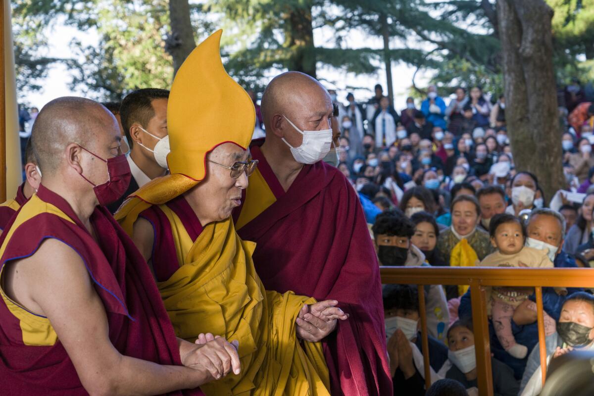 The Dalai Lama, wearing a ceremonial yellow hat, arrives at a temple to give a sermon.