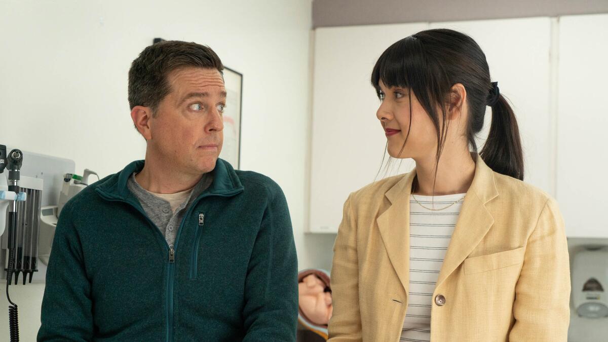 Ed Helms and Patti Harrison look at each other in an exam room.