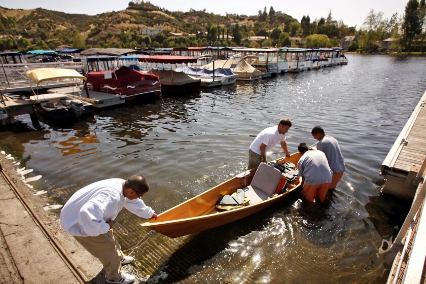 A teacher helps students launch a solar-powered boat in the lake.