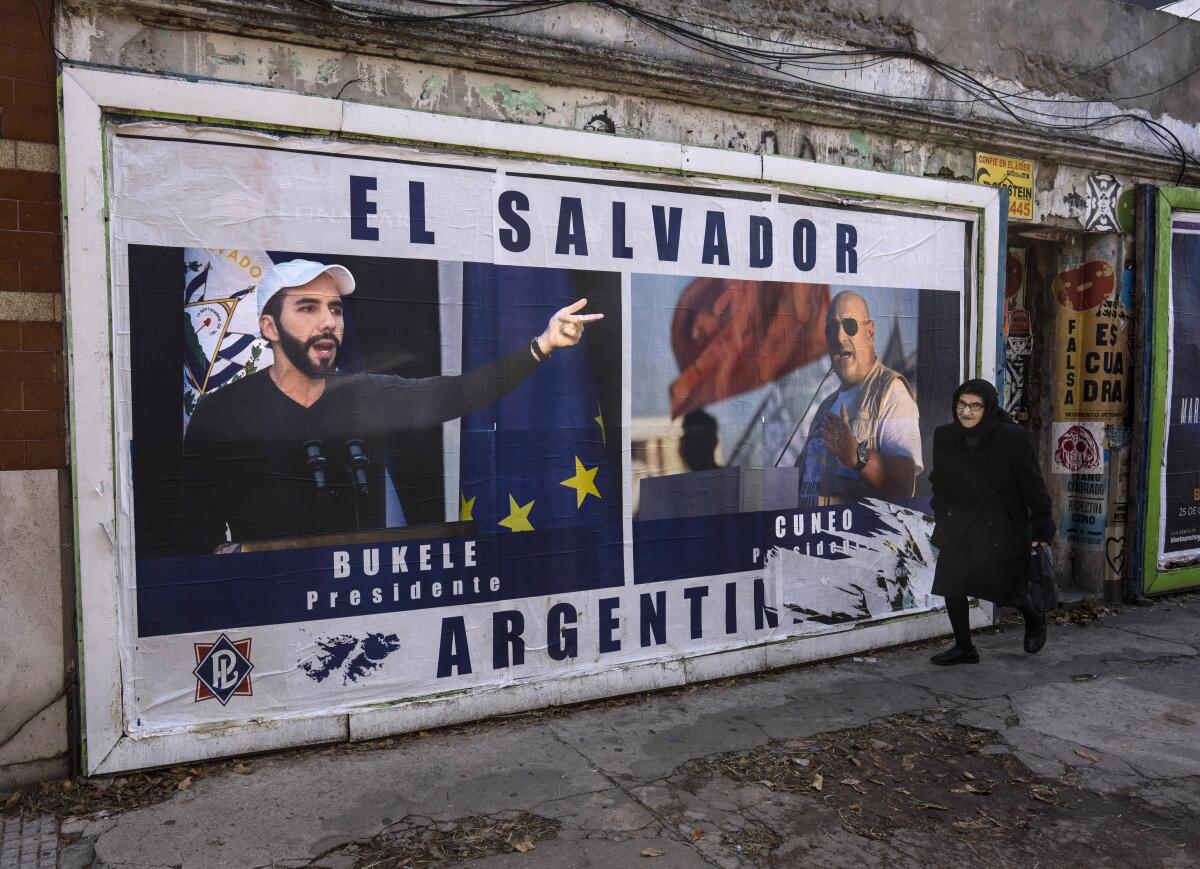 A woman walks past a billboard of a bearded man in white cap, left, and another man, with the words El Salvador and Argentina