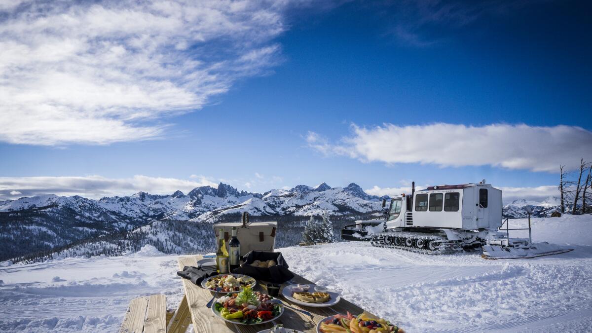 A mountaintop view with a picnic in the foreground and a snowcat in the background.