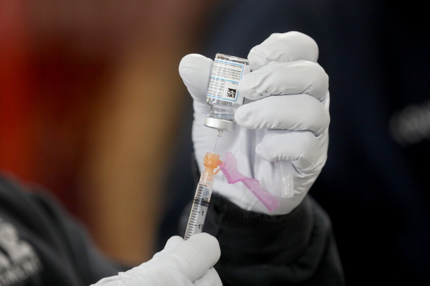 A close-up of gloved hands holding a syringe and vial of vaccine.