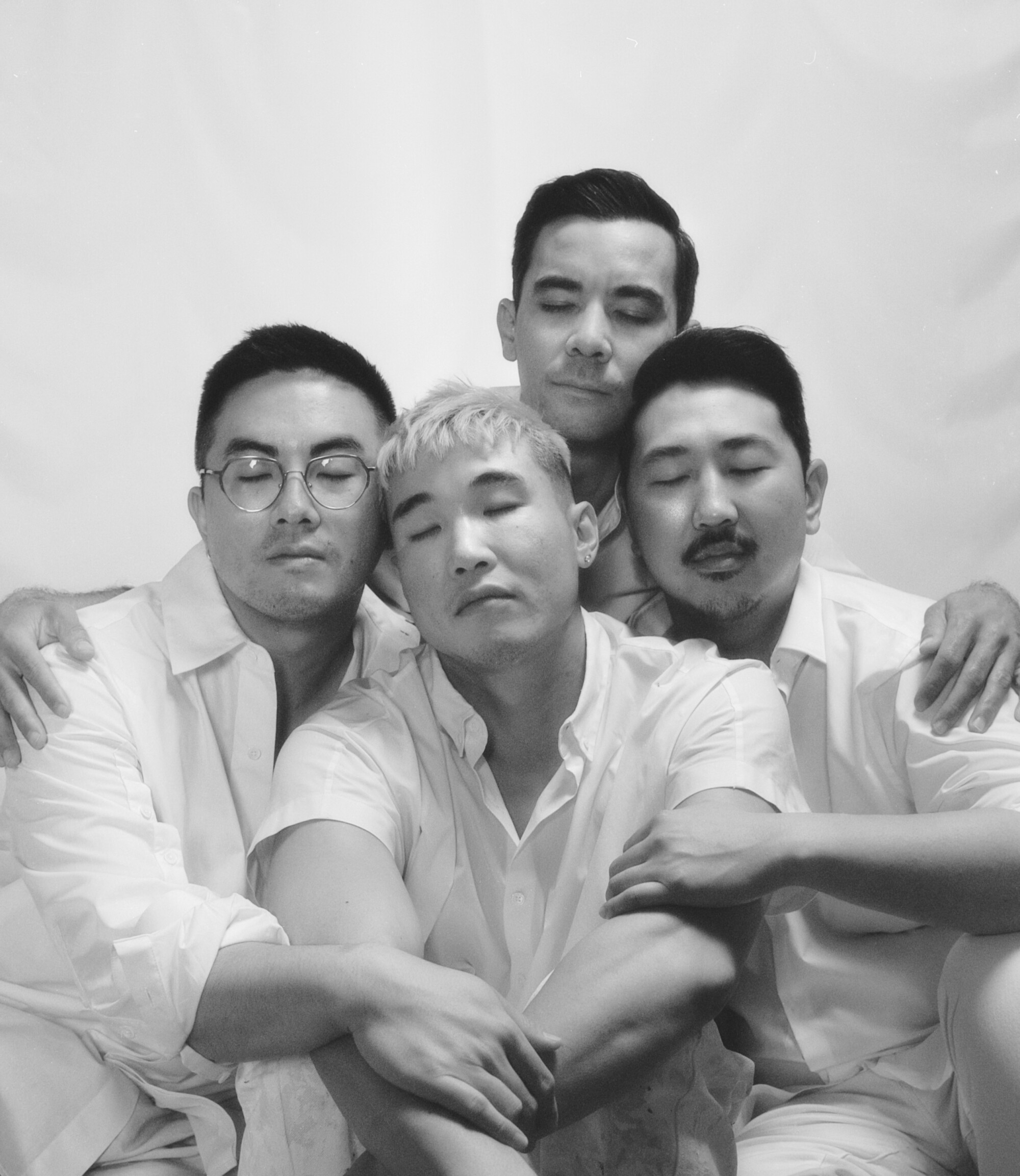 Four men in white embrace and close their eyes in a black and white photo
