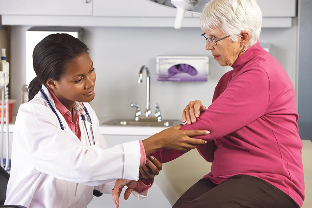 A younger doctor examines an older patient’s arm