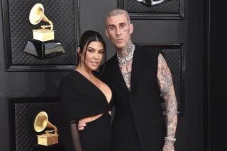 A heavily tattooed man puts his arm around the waist of a woman in a black gown