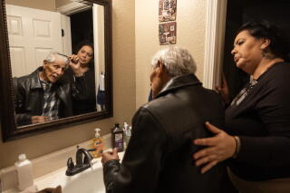 Caretaker Maria Dominguez helps Bob Fernandez get ready before a morning walk in Lodi, Calif.