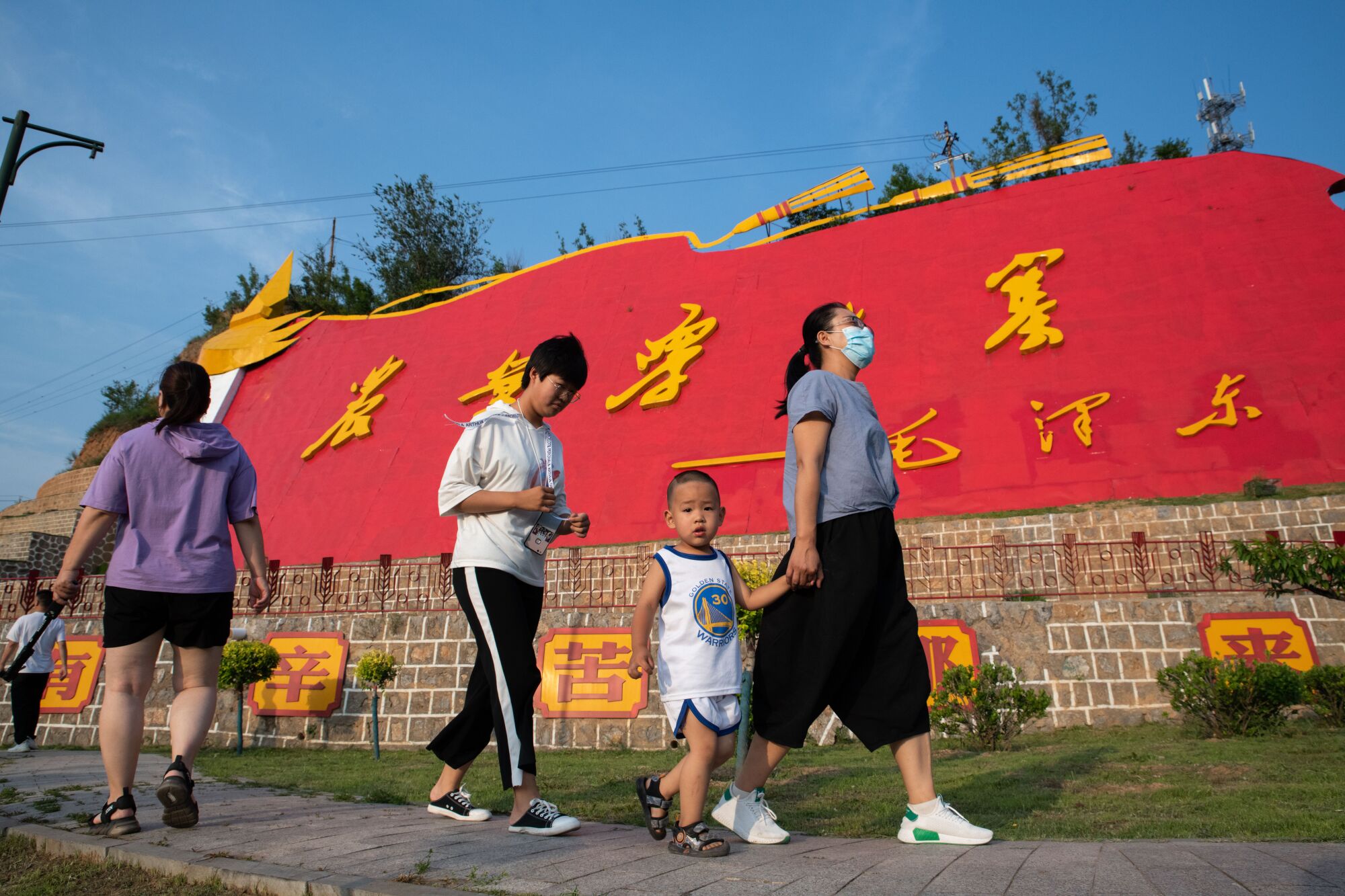 People walk past a large red banner with Chinese characters in gold stretching across a wall