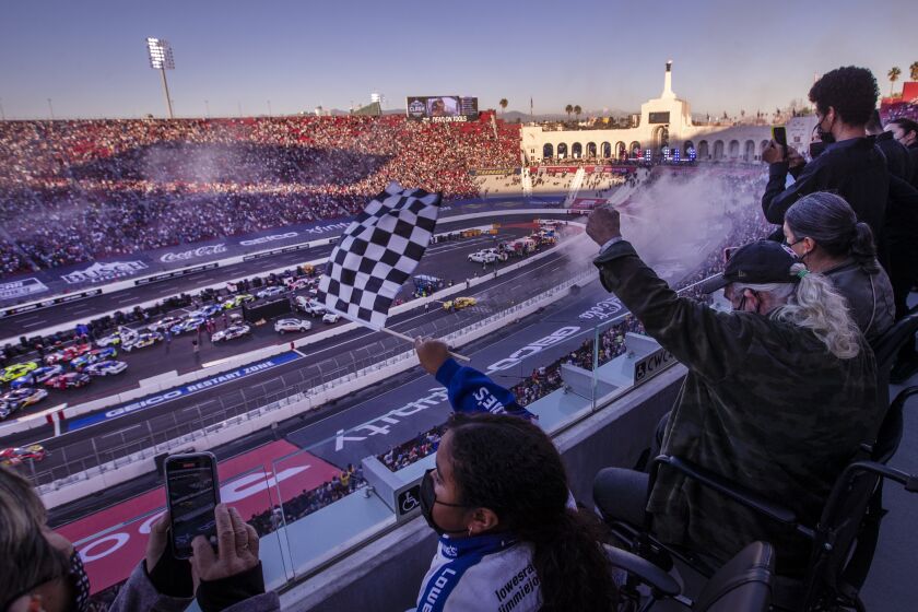 Los Angeles, CA - February 06: Amaya DiBella, 8, center, waves the checkered flag as her grandparents, Vice DiBella, left, and John DiBella, right, and mom Inez DiBella, cheer as NASCAR driver Joey Logano, #22, does a celebratory burn-out victory lap after he won the Busch Light Clash At The Coliseum, a NASCAR exhibition race Sunday, Feb. 6, 2022. The season-opening Clash exhibition race gets a taste of West Coast flavor in 2022, marking a historic first visit to the tradition-rich Los Angeles Memorial Coliseum. The event is to be contested around a quarter-mile asphalt oval that will be built around the facility's football field. The Los Angeles event marks the first time the preseason Clash is held outside of Daytona International Speedway since its inception in 1979, and gives the sport its first competitive look at the Next Gen car on Feb. 6 in a non-points event, including a pre-race concert by Pit Bull. Photo taken at LA Memorial Coliseum on Sunday, Feb. 6, 2022 in Los Angeles, CA. (Allen J. Schaben / Los Angeles Times)