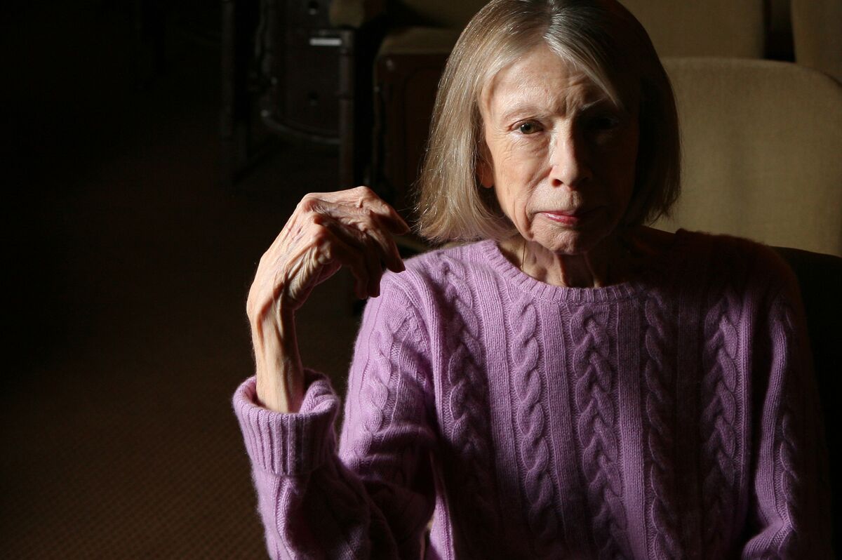 Joan Didion posing in a cable-knit purple sweater