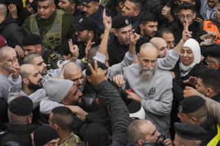 Palestinian prisoners in gray gesture as they are greeted by a crowd.