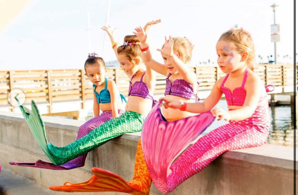 Mini mermaids sit on Balboa Island seawall during an outdoor summer event held by Once Upon An Island.