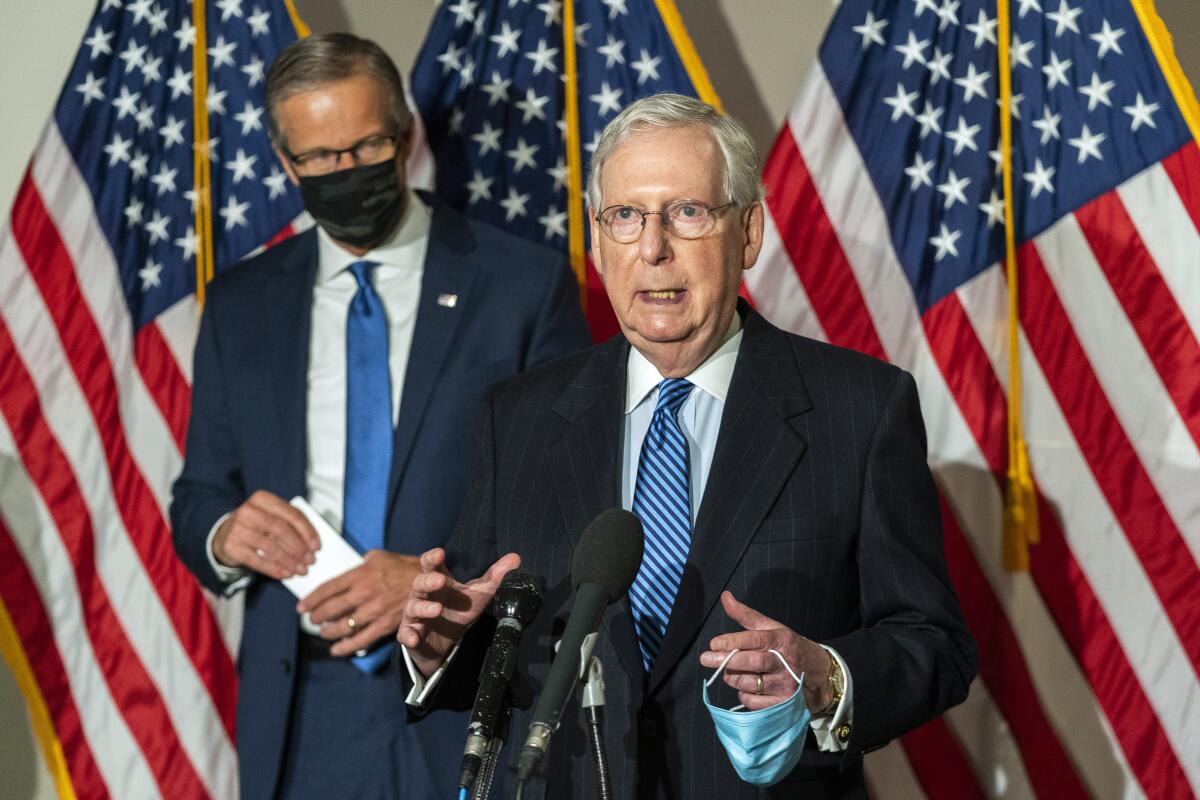 Senate Majority Leader Mitch McConnell (R-Ky.), with Sen. John Thune (R-S.D.), stands before American flags.