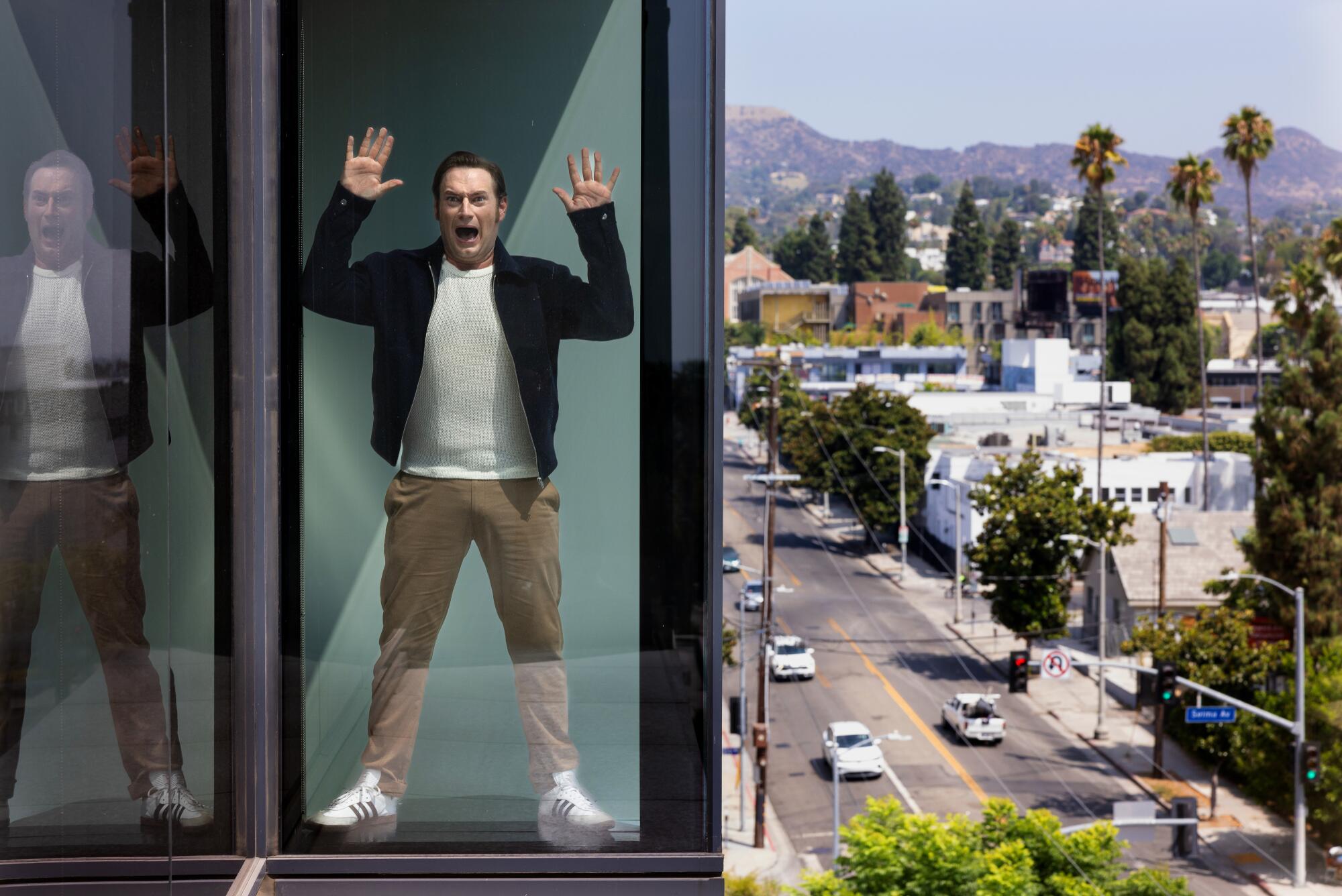A man wearing a dark jacket, white T-shirt and khaki pants is seen shouting through a glass wall.