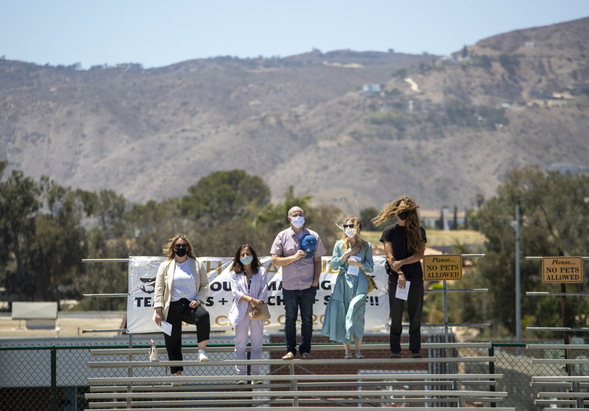 Five people stand on a bleacher with rolling hills in the background.