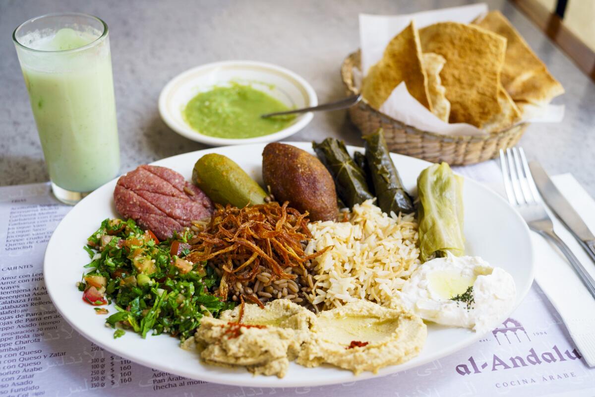 A spread of Lebanese food on a plate next to a green drink, green sauce and bowl of tortilla chips.