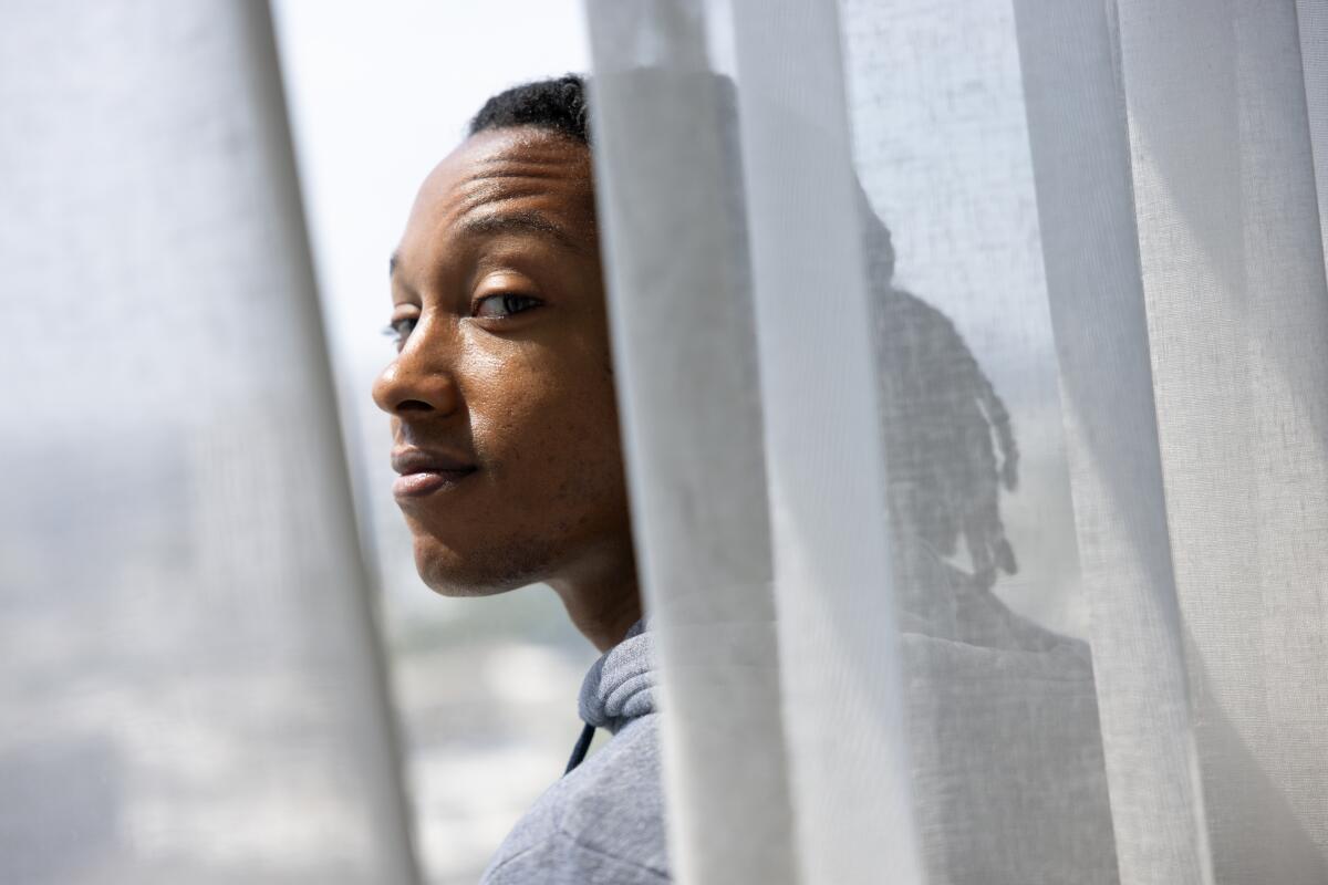 Young black man standing behind a sheer curtain