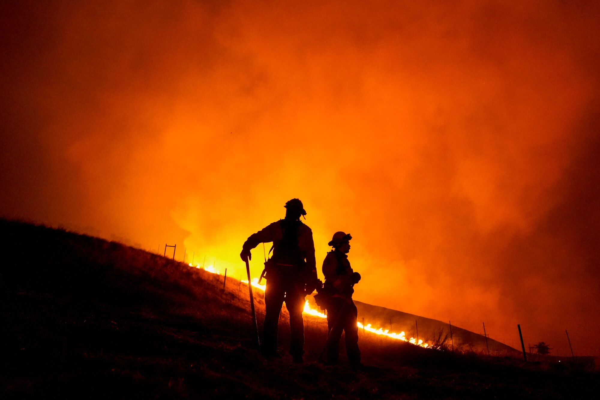 Members of the Santa Rosa Fire Department stand before a hill in flames.