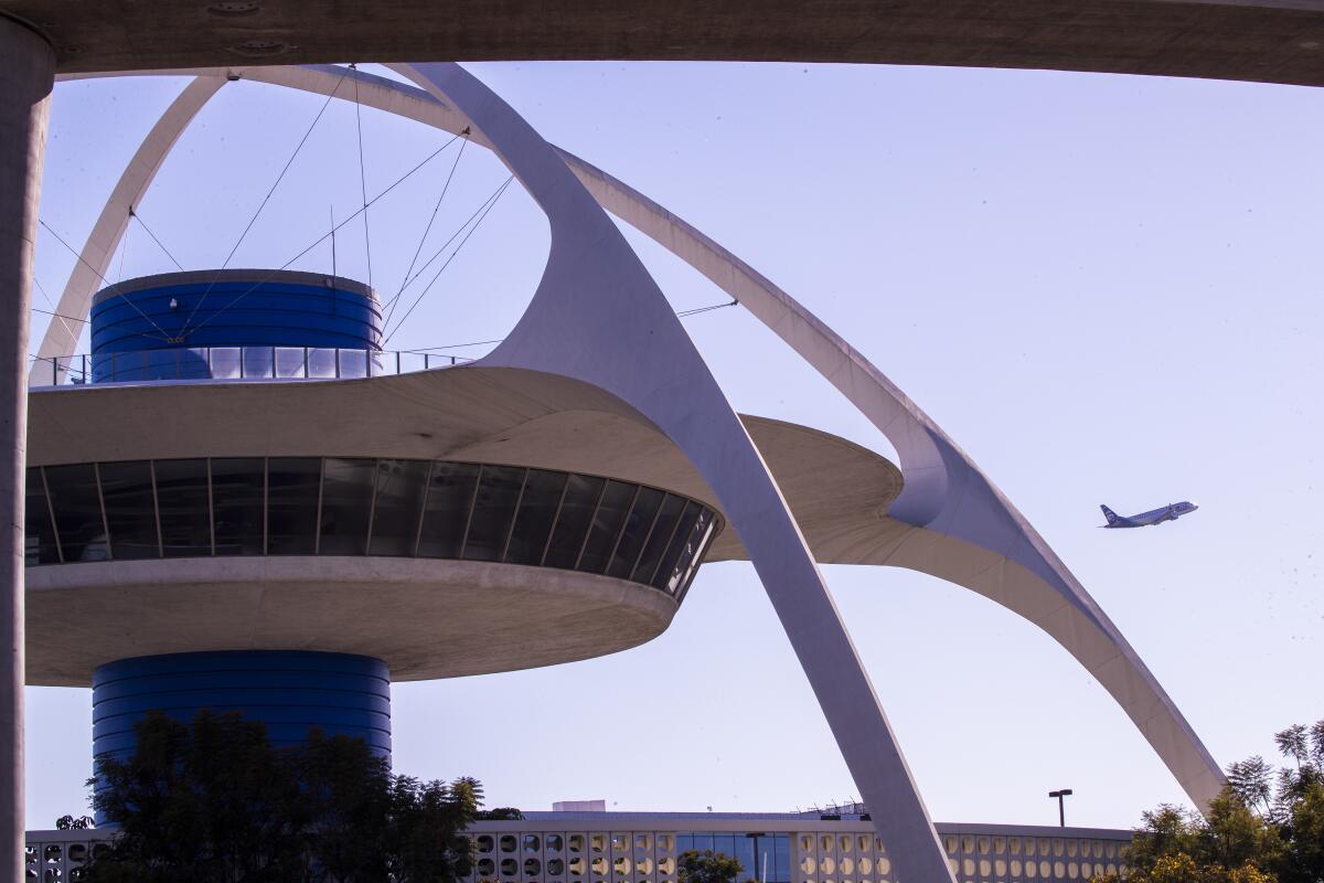 A plane flies away from LAX with the airport's Theme Building in the foreground