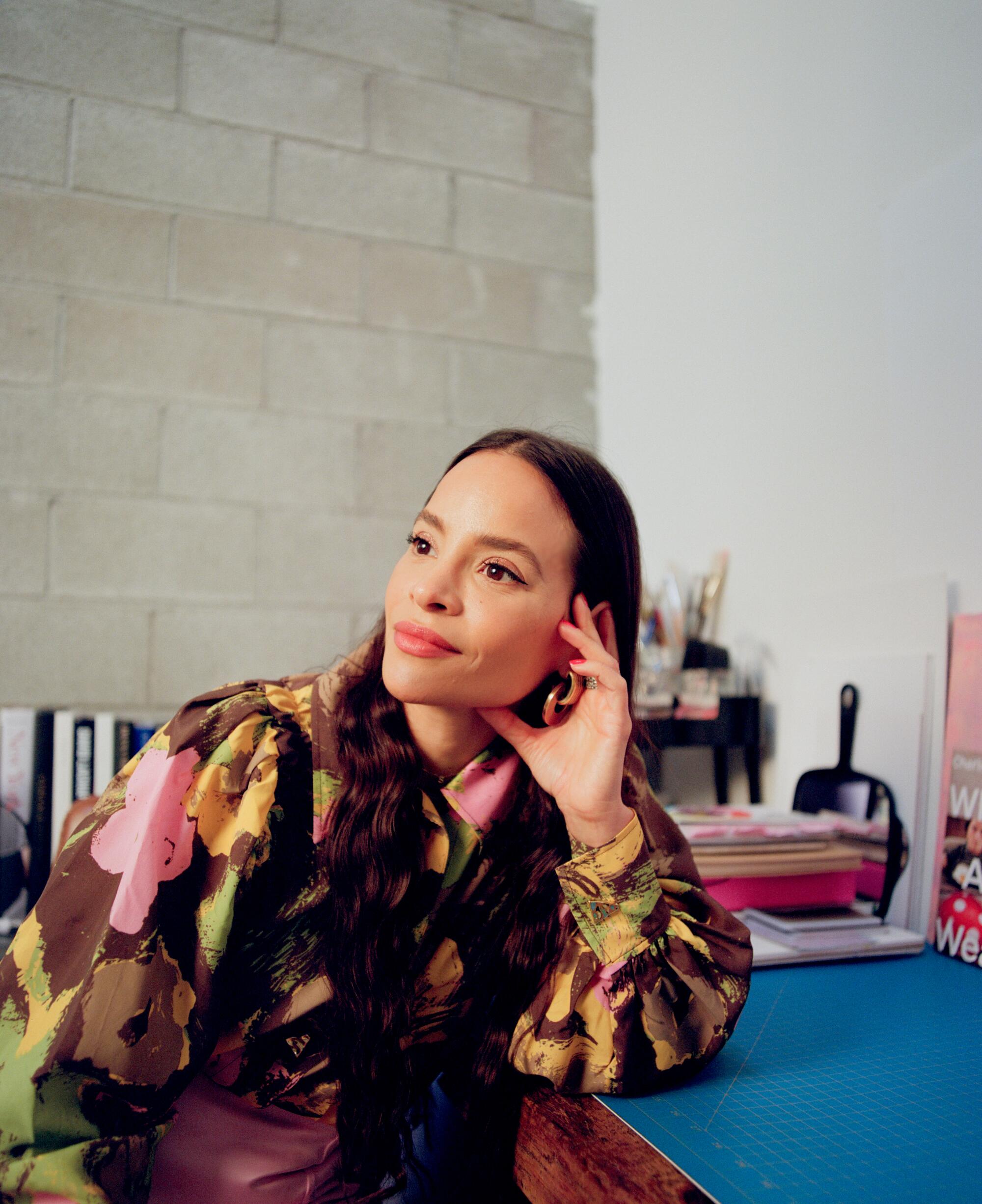 Sophie Lopez, wearing a colorful blouse, leans her head toward her hand, her elbow resting on a desk.